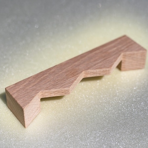 May include: A small, light brown wooden object with a stepped design. The object appears to be a decorative or functional piece, possibly for home decor or woodworking projects. The wood grain is visible, indicating a natural material.