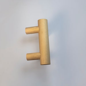 Può includere: Un pomello per armadio in legno con un design rettangolare semplice. Il pomello è realizzato in legno chiaro e ha una finitura liscia.