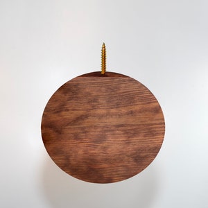 May include: A round wooden wall mount with a screw in the center. The wood is a dark brown color with a natural wood grain.