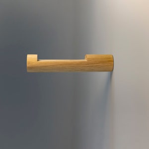 May include: A wooden toilet roll holder mounted on a wall. The holder is made of light brown wood and has a simple, modern design.