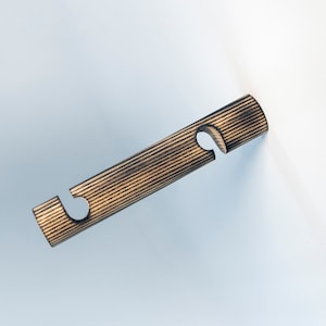 May include: A wooden wall-mounted hook with a striped pattern and two cut-out hooks. The hook is brown and black.
