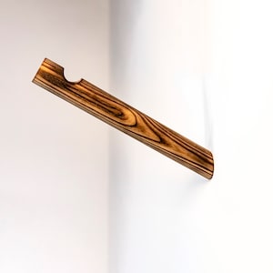 May include: A wooden dowel rod with a cut-out section, mounted on a white wall. The rod is brown with dark brown wood grain.