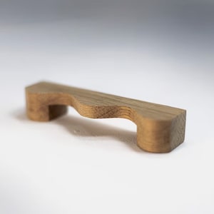 May include: A wooden drawer pull with a wavy, organic shape. The pull is made of light brown wood and has a smooth, polished finish.