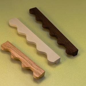 May include: Three wooden drawer pulls with a scalloped edge. The pulls are in different shades of brown and white.