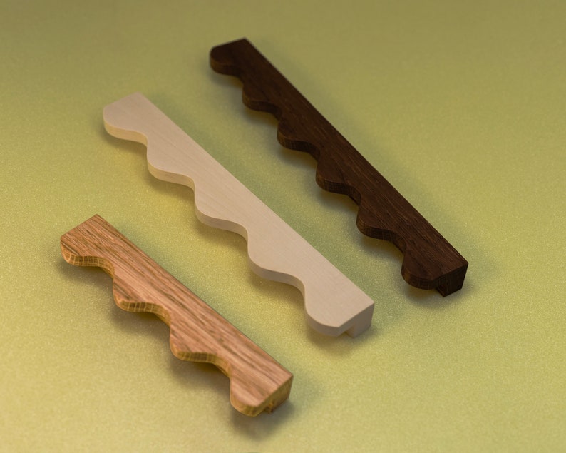 May include: Three wooden drawer pulls with a scalloped edge. The pulls are in different shades of brown and white.