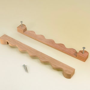 May include: Two wooden handles with a wavy edge and a screw on each end. The handles are light brown and are on a light yellow background.