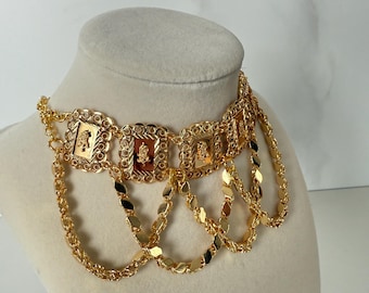 May include: A gold-toned choker necklace with multiple chains and square-shaped pendants. Each pendant features a raised design.