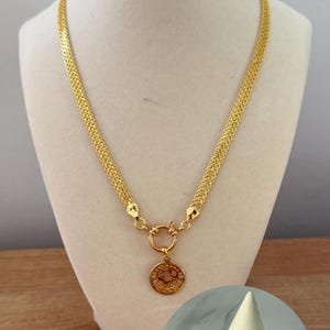 May include: A gold-colored necklace with a woven chain design and a circular pendant featuring an embossed design. The necklace is displayed on a mannequin. A matching bracelet with a similar pendant is also shown.