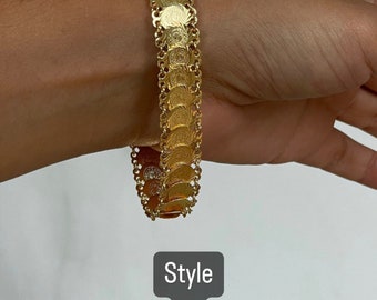 May include: Gold bracelet with a chain design featuring a series of round, coin-shaped charms. The bracelet is on a person's wrist. Style 1.