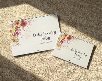 May include: Two spiral-bound wall calendars with white covers featuring watercolour floral illustrations in shades of red, orange, and yellow. The text reads Becky Hemsley Poetry 2027 Calendar in black script and sans-serif font.