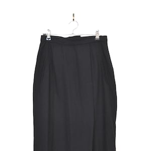 May include: A black skirt suspended from a hanger. The skirt is a plain black colour and seems to be made of a woven material. It has a straight shape with a small overlap at the front and pockets on the sides. The skirt is a midi length.