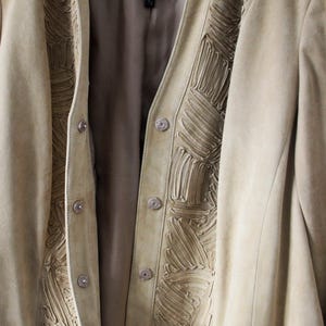May include: A tan suede jacket with decorative stitching along the front and collar. The jacket has a button-up closure and a soft, neutral color, perfect for layering. The label reads "LAFAYETTE 148".