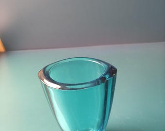 May include: A small, turquoise-colored glass vase with a unique, asymmetrical shape. The vase has a wide, rounded opening and tapers down to a narrow base. The glass is transparent, allowing light to pass through, and has a smooth, polished finish.
