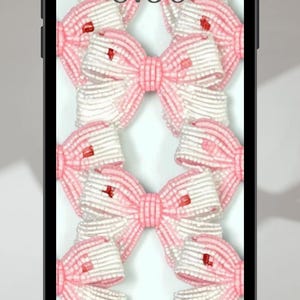 May include: A close-up of a smartphone screen displaying a pink and white bow pattern with red accents. The time 8:30 is displayed on the screen.
