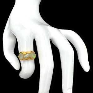 Op de afbeelding: Een gouden ring met drie witte opaalstenen gezet in een getextureerde band.