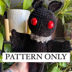 Könnte beinhalten: Häkelmuster für eine schwarze Fledermaus mit roten Augen und einem grauen Pelzkragen. Das Muster ist für ein Plüschtier und ist mit "PATTERN ONLY" gekennzeichnet.