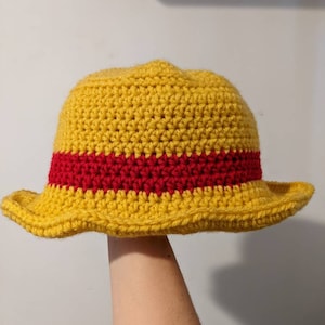 May include: A yellow crocheted hat with a red stripe around the crown. The hat has a wide brim and is made with a simple stitch pattern.