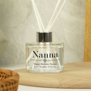 May include: A clear glass diffuser bottle with a silver cap and white diffuser sticks. The bottle has a label that reads "Nanna" with a decorative design and the text "Happy Birthday Nanna Love Stephen & Lynn".