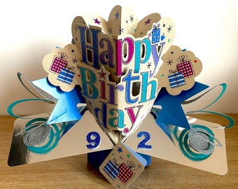 May include: A pop-up birthday card with the words "Happy Birthday" in blue and purple. The card has a blue and silver color scheme with the number "92" displayed. Gift box illustrations are also present.