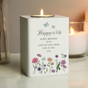Op de afbeelding: Witte vierkante kaarsenhouder met een theelichtje erin. De houder heeft een bloemmotief met vlinders en de tekst "Happy 65th Happy Birthday June Lots of Love from Iain & Gill XXX".