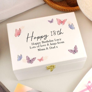 May include: A white wooden box with a gold clasp, adorned with pastel butterflies. The box is inscribed with "Happy 18th" and a personalized birthday message. A decorative gift box for a special occasion.