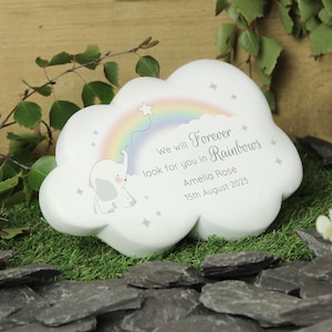 Puede incluir: Una placa blanca con forma de nube que presenta un arcoíris pastel, un pequeño elefante gris y estrellas grises. El texto dice: We will Forever look for you in Rainbows, Amelia Rose, 15th August 2023. El diseño está impreso sobre una superficie mate.