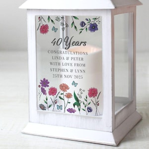 May include: White wooden lantern with glass panels, featuring floral and butterfly designs. The front panel displays the text "40 Years Congratulations Linda & Peter With Love From Stephen & Lynn 25th Nov 2025". A candle is visible inside.