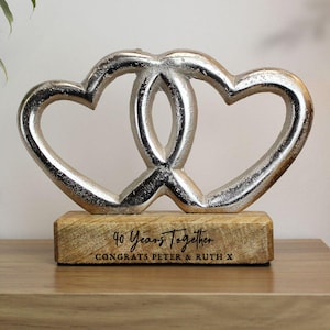 Può includere: Scultura argentata di due cuori intrecciati su una base di legno. La base è incisa con la scritta "40 Years Together" e "Congrats Peter & Ruth X". Un oggetto decorativo per celebrare un anniversario di matrimonio.