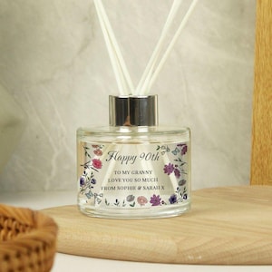 May include: A clear glass diffuser bottle with a silver cap and white reeds. The bottle is decorated with floral designs and the text "Happy 90th, To my Granny, Love you so much, From Sophie & Sarah X."