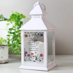 Op de afbeelding: Witte lantaarn met een bloemenontwerp en het woord "Mum" op het glas gedrukt. De lantaarn bevat de tekst "ALWAYS MY MUM FOREVER MY FRIEND LOTS OF LOVE CHARLOTTE X".
