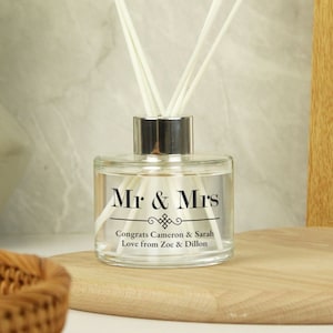 Puede incluir: Una botella de difusor de vidrio transparente con una tapa plateada y texto negro que dice "Mr & Mrs" con un diseño decorativo y el texto "Congrats Cameron & Sarah Love from Zoe & Dillon".