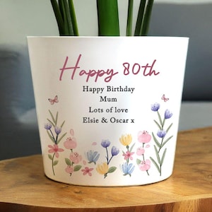 Può includere: Vaso di fiori in ceramica bianca con la scritta rosa "Happy 80th". Decorato con fiori ad acquerello rosa, blu e gialli, e il testo "Happy Birthday Mum, Lots of love, Elsie & Oscar x".