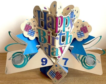 May include: A pop-up birthday card with a blue, pink, and green "Happy Birthday" message. The card is decorated with stars and presents. The numbers 9 and 7 are visible on the card.