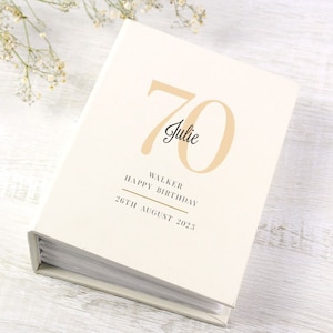May include: A white photo album with a gold inscription that reads "70 Julie Walker Happy Birthday 26th August 2023".