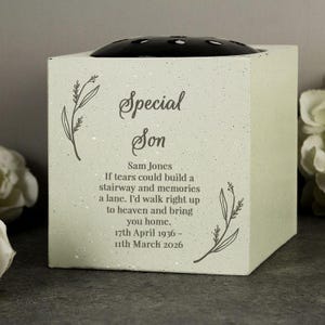 May include: A square, light green memorial flower vase with a black top. The front features the text "Special Son" and a poem, along with the name Sam Jones and dates 17th April 1936 - 11th March 2026. Floral illustrations are on the sides.