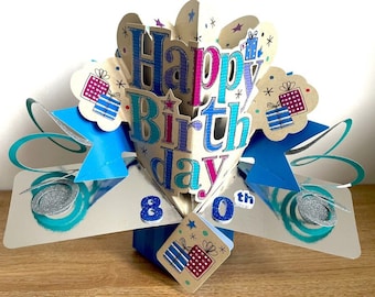 Puede incluir: Una tarjeta emergente azul y plateada con las palabras "Happy Birthday" en letras de colores y el número "80" en la parte delantera. La tarjeta está decorada con regalos y estrellas.