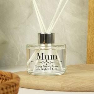 Può includere: Una bottiglia di diffusore in vetro trasparente con un tappo argentato e canne nere. La bottiglia ha un'etichetta con la scritta "Mum Happy Birthday Mum Love Stephen & Lynn".