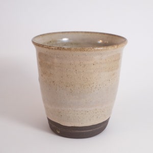 May include: A ceramic mug with a light brown glaze and a dark brown rim. The mug has a speckled appearance and a slightly rounded shape.