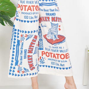 May include: Cream culottes featuring a vintage potato sack design. The print includes the words "Sweet Kitten Brand Potatoes" and a cat graphic. The culottes are printed with blue hearts and red accents. The product is made in the U.S.A.