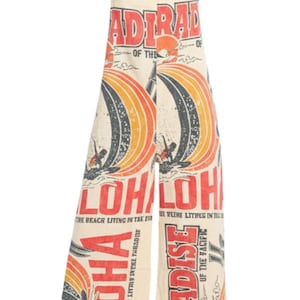 May include: Cream-colored jumpsuit with a vintage-style print featuring surfers, rainbows, and the words "Aloha" and "Paradise." The jumpsuit has wide legs and adjustable straps, evoking a retro beach vibe.