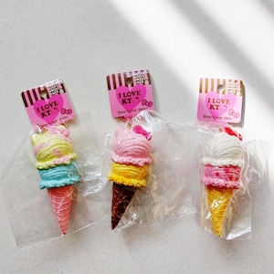 May include: Three colorful ice cream cone-shaped keychains. Each keychain is packaged in a clear plastic bag and features a pink tag with the text "I LOVE KT" and "Don't eat this!". The ice cream has multiple layers of different colors.