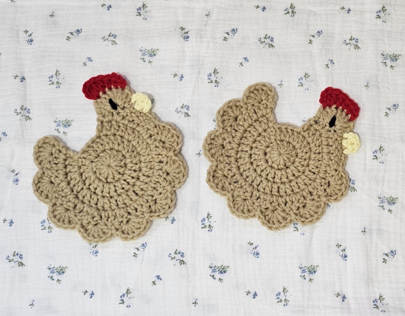 Puede incluir: Dos posavasos hechos a mano de ganchillo con forma de gallina. Los posavasos son de color beige con una cresta roja y una peque&ntilde;a car&uacute;ncula amarilla. Se colocan sobre un fondo blanco con un estampado floral azul.