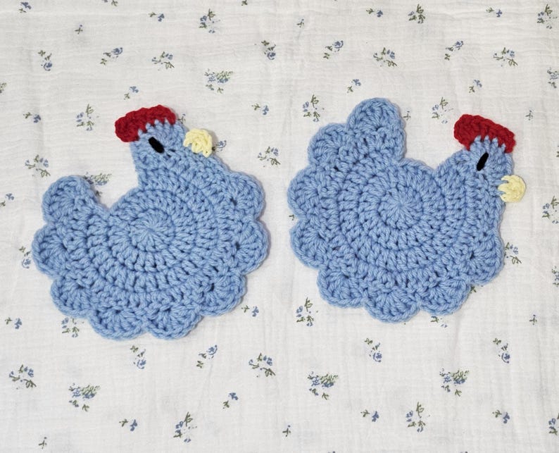 Puede incluir: Dos salvamanteles hechos a mano, de ganchillo azul con forma de gallina. Cada salvamanteles tiene una cresta roja, una car&uacute;ncula amarilla y un peque&ntilde;o ojo negro. Est&aacute;n sobre una tela blanca con un delicado estampado floral.