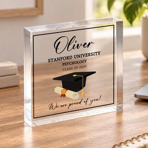 May include: A clear acrylic block featuring the printed text Oliver, Stanford University, Psychology, Class of 2026, and We are proud of you. The design includes a black graduation cap and a rolled diploma with a red seal tied with a ribbon.