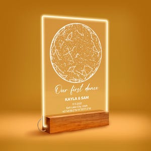 May include: A rectangular clear acrylic plaque with a glowing yellow edge, featuring a white engraved star map. Below the map, the text reads: Our first dance, KAYLA & SAM, 11.11.2021, Salt Lake City, Utah, 40°45'38.2"N 111°53'17.2"W. It sits on a wooden base.