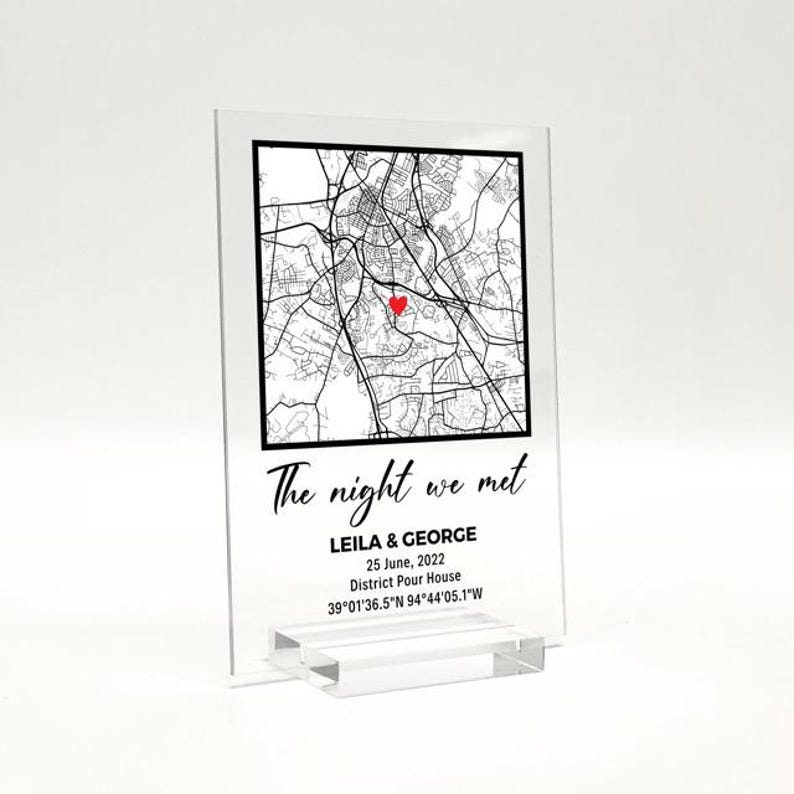 May include: A clear acrylic map print featuring a black and white city map, a red heart marking a location, and the text "The night we met." Below, it reads "LEILA & GEORGE, 25 June, 2022, District Pour House, 39&deg;01'36.5"N 94&deg;44'05.1"W."
