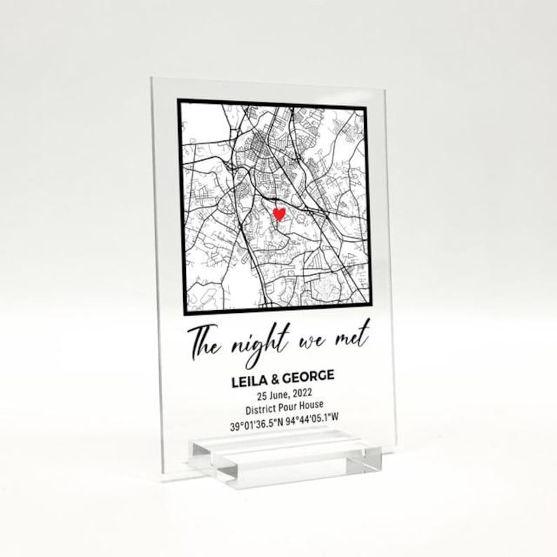Może przedstawiać: Przezroczysty nadruk na akrylu z czarno-białą mapą miasta, czerwonym sercem oznaczającym lokalizację i tekstem "The night we met". Poniżej napis "LEILA & GEORGE, 25 czerwca 2022, District Pour House, 39&deg;01'36.5"N 94&deg;44'05.1"W."