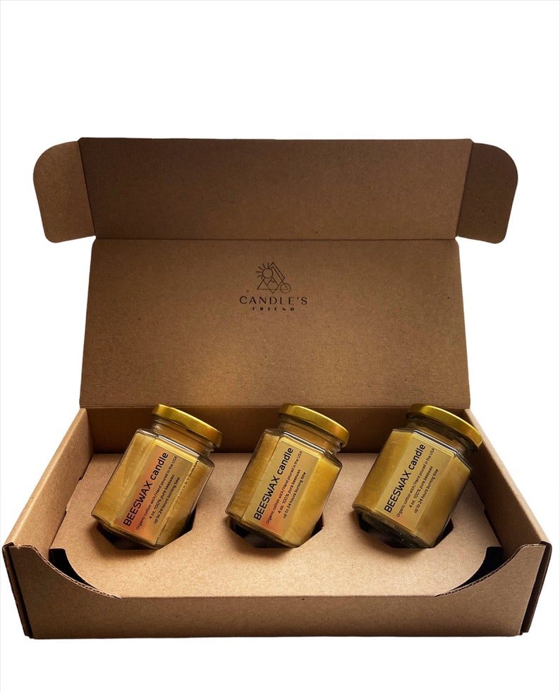 May include: Three glass jars filled with beeswax candles in a brown cardboard box. The jars have gold lids and labels that say "BEESWAX candle" with a description of the candle. The box has a logo that says "CANDLE'S FRIEND".