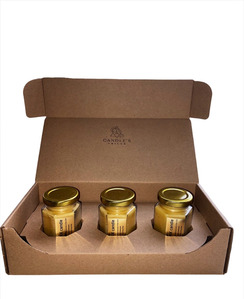 May include: Three small glass jars with gold lids containing yellow wax candles. The jars are in a brown cardboard box with the words "CANDLE'S" printed on the inside.
