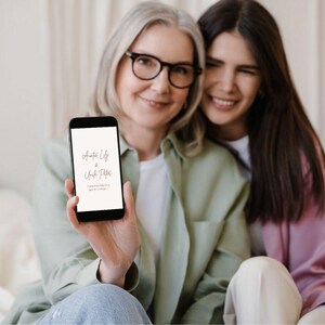 May include: A black smartphone showing the text "Auntie Lily & Uncle Peter" in a stylish script. The phone is held by a person wearing glasses and a light green shirt, with another person smiling beside them. The background is soft and blurred.